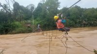 Petugas PLN saat membenahi jaringan kabel listrik yang terhantam banjir di atas jembatan gantung. (DETAIL/Daryanto)