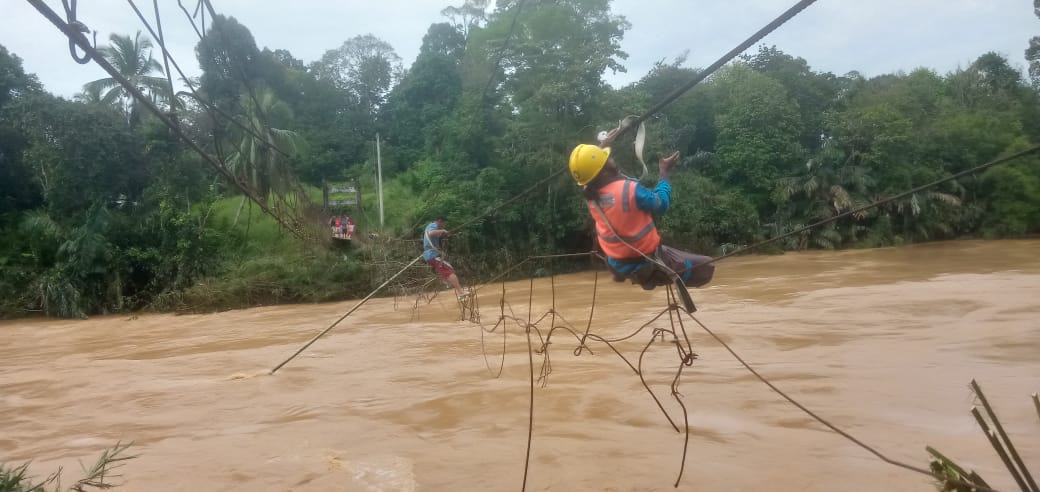 Petugas PLN saat membenahi jaringan kabel listrik yang terhantam banjir di atas jembatan gantung. (DETAIL/Daryanto)